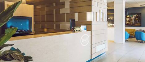 A hotel reception desk with a modern design, a digital screen, and a sign indicating the hotel name.