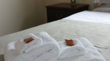 A neatly made bed with white linens and a pair of folded towels with brown tags on a hotel room.
