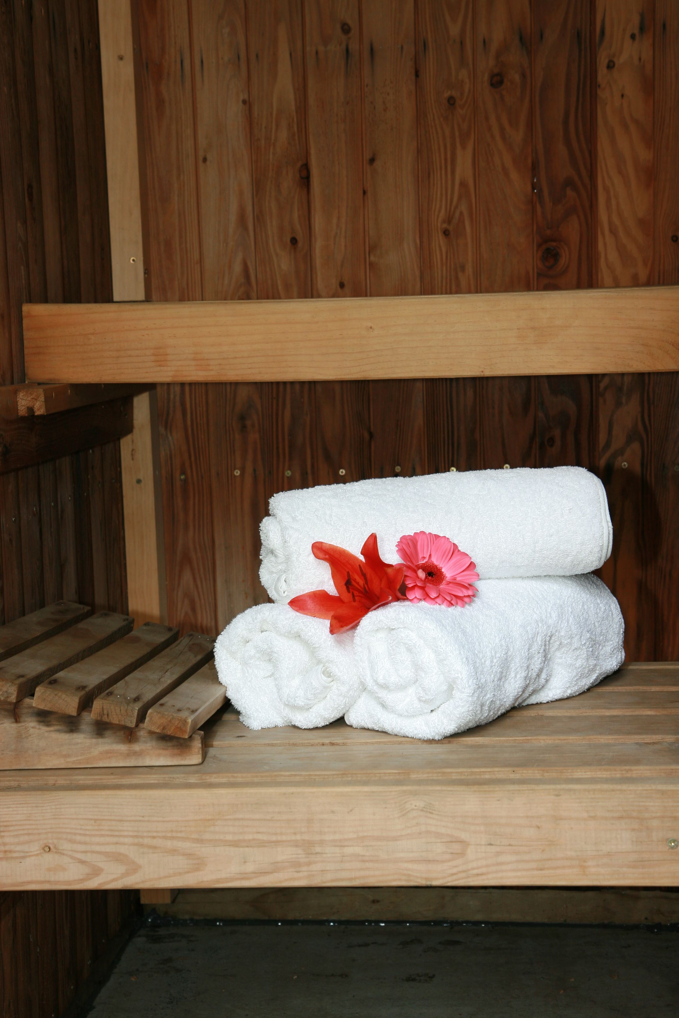 A wooden bench with two rolled white towels and a pink flower on it.