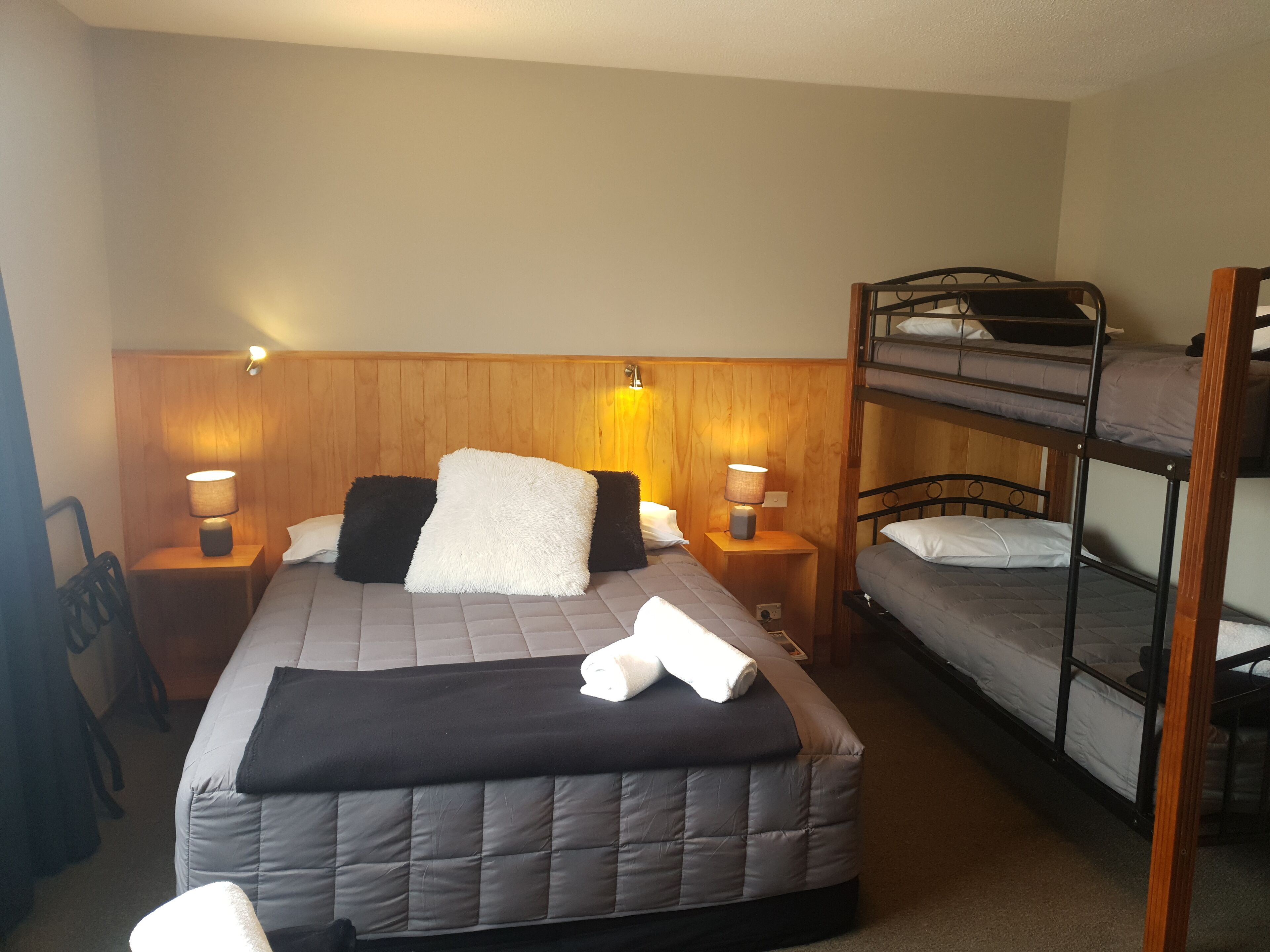 A bedroom with a single bed, two bedside tables with lamps, a bunk bed, and a wooden headboard.