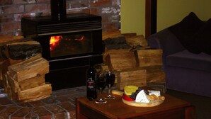 A cozy living room with a brick fireplace, a stack of firewood, a wooden table with a cheese platter, wine glasses, and a couch. - Abisko Lodge (Methven)