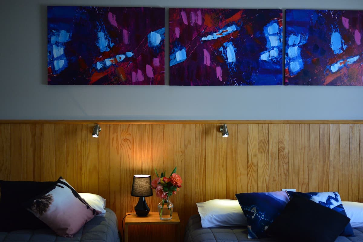 Quarto de hotel com duas camas, painéis de madeira nas paredes, mesa de cabeceira com abajur e um vaso de flores.