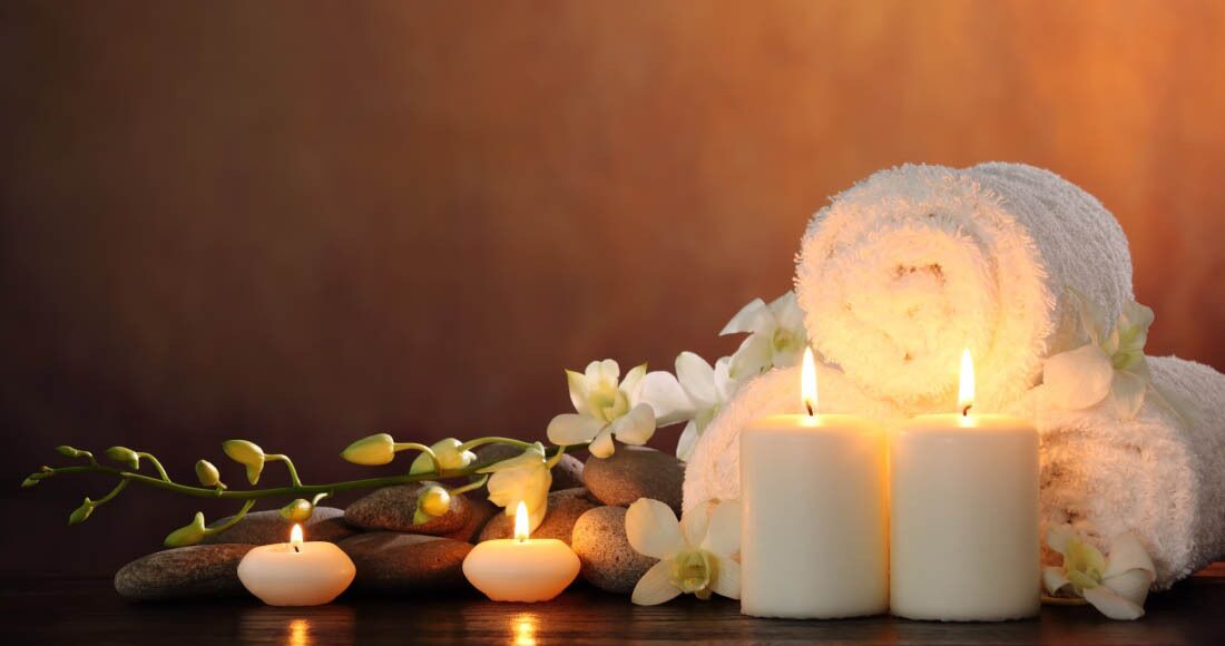 A spa setting with candles, a rolled towel, and flowers.