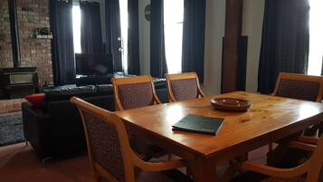 A living room with a wooden dining table, four chairs, a black leather sofa, a TV, and a fireplace.