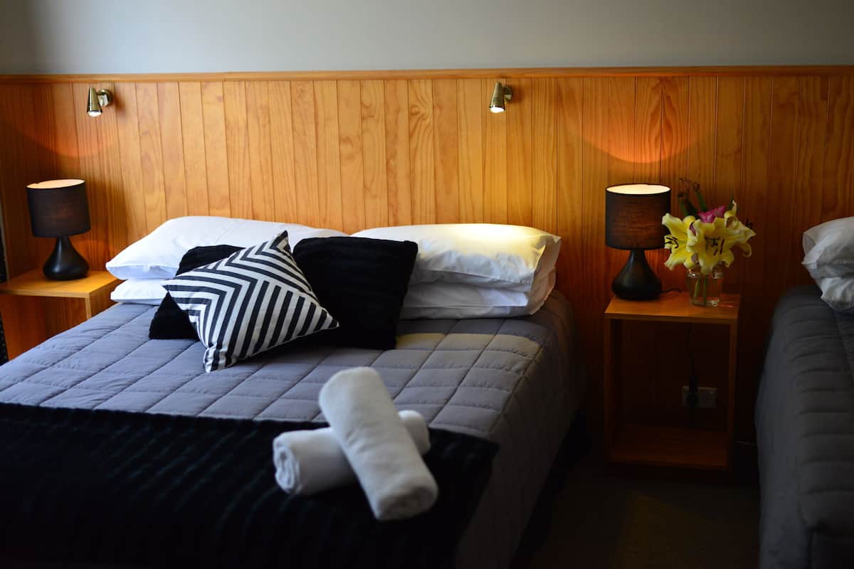 Cama bem arrumada com travesseiro listrado, um travesseiro branco e duas toalhas enroladas. Há duas luminárias de cabeceira e um vaso com flores em uma mesa de cabeceira.