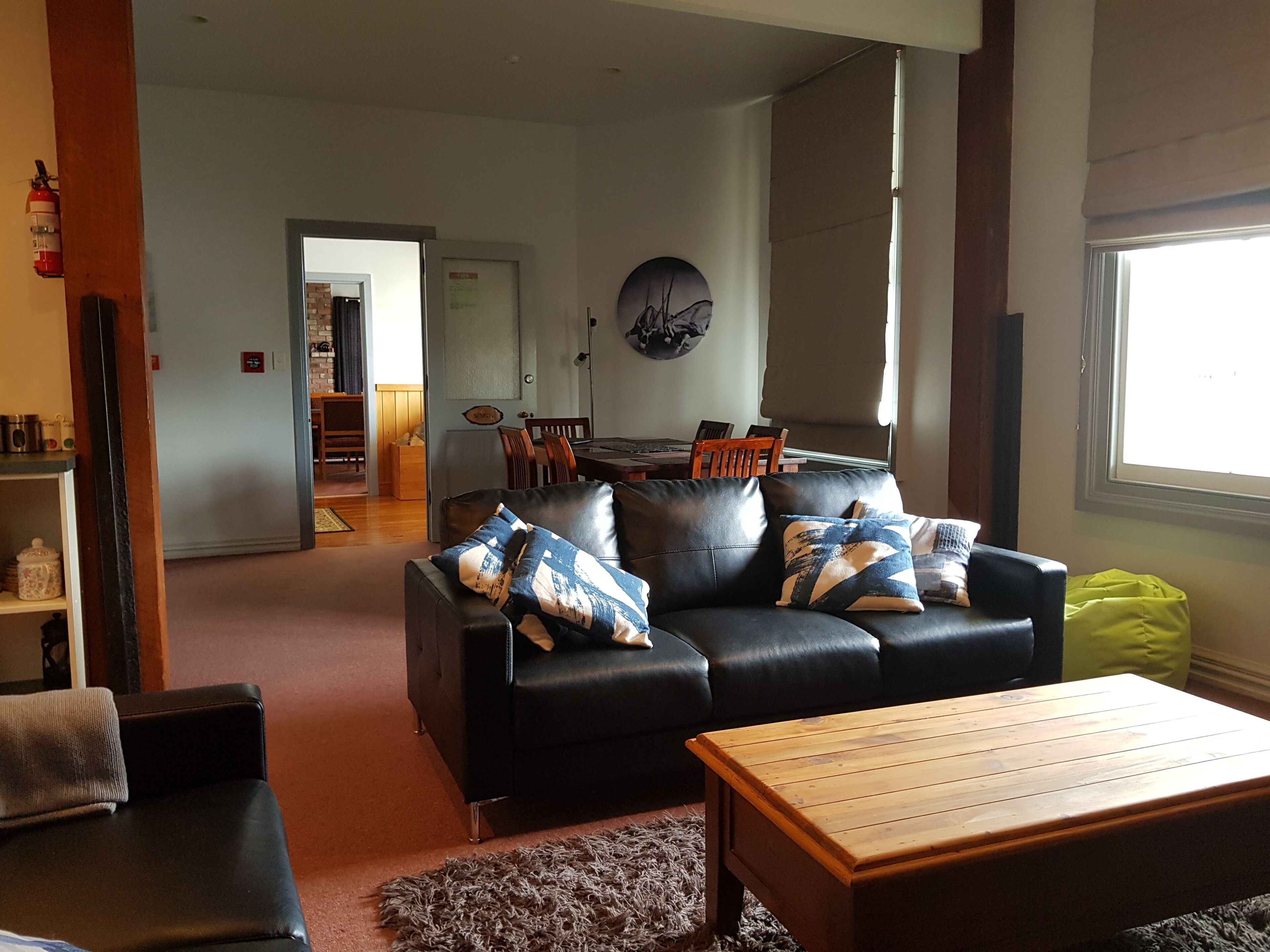 A living room with a black leather sofa, wooden coffee table, and a dining area in the background.