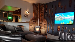 A cozy living room with a fireplace, a TV displaying a scenic view, and various cultural masks on the wall. - Abisko Lodge (Methven)