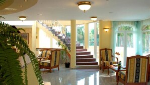 A spacious lobby with a staircase, wooden chairs, and a large plant. - SANTE Hévíz (Hévíz)