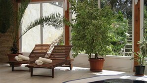 A spa area with a hot tub, two wooden lounge chairs, and potted plants. - SANTE Hévíz (Hévíz)