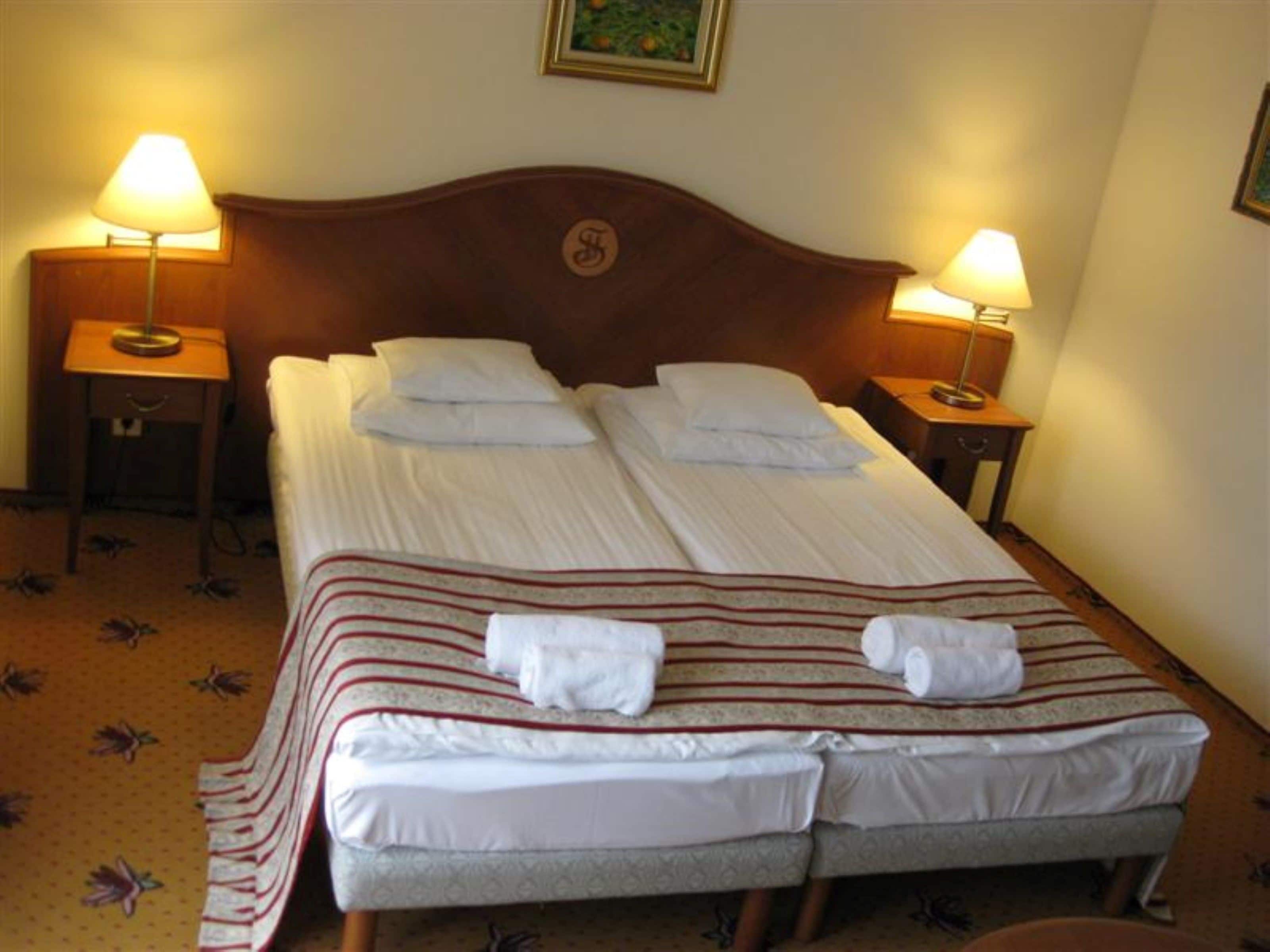 A neatly made double bed with white linens and striped blankets, two bedside lamps, and a framed picture on the wall.