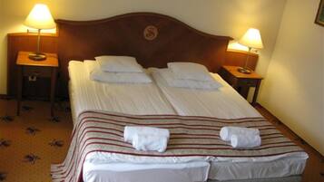 A neatly made double bed with white linens and striped blankets, two bedside lamps, and a framed picture on the wall.
