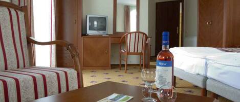 A hotel room with a bed, a desk with a television, a chair, and a bottle of wine.