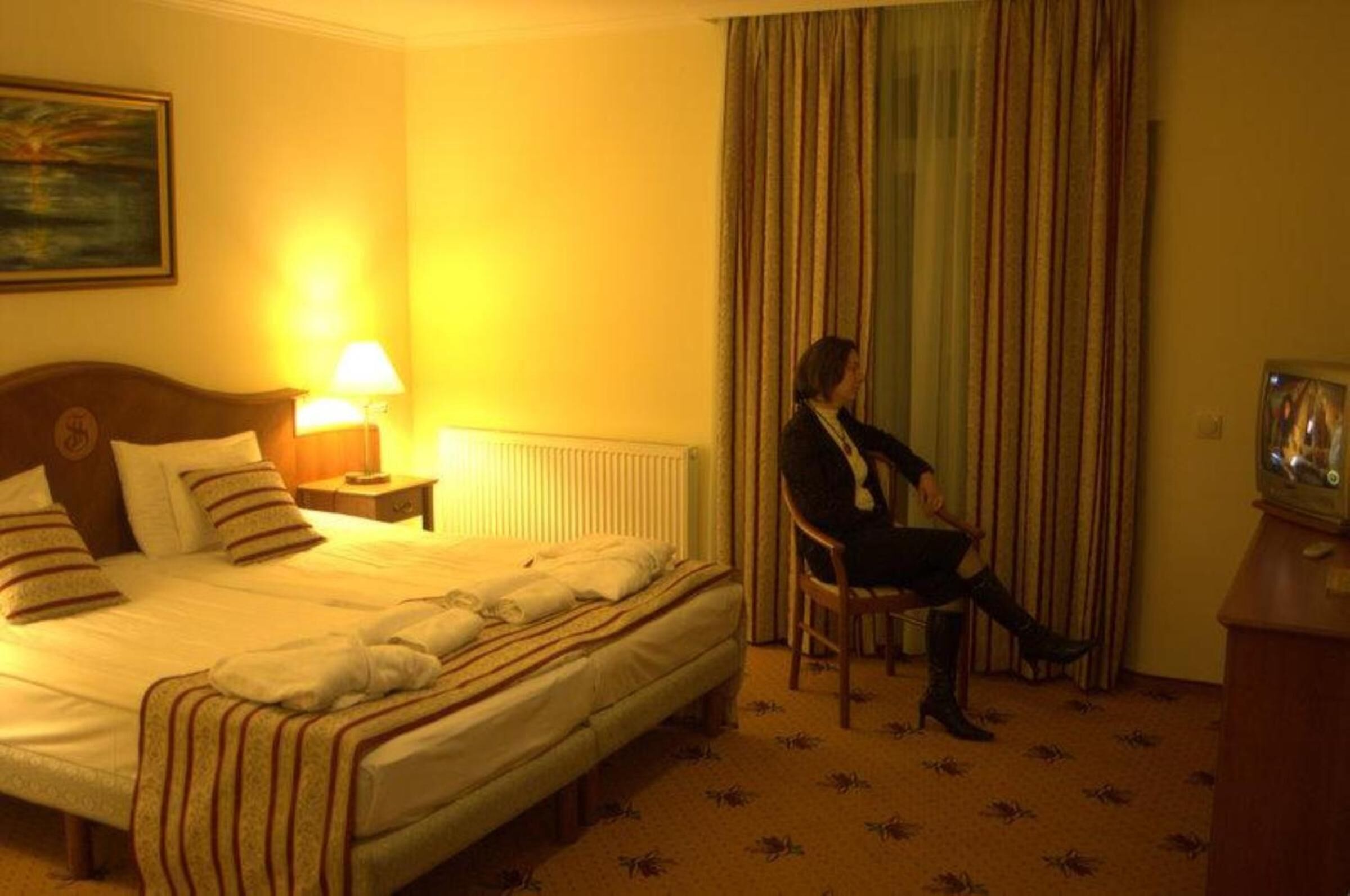 Una habitación de hotel con una cama, una silla, una lámpara y un televisor.