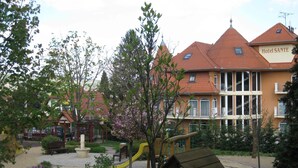 A hotel with a red-tiled roof, a playground with a yellow slide, and a bench. - SANTE Hévíz (Hévíz)