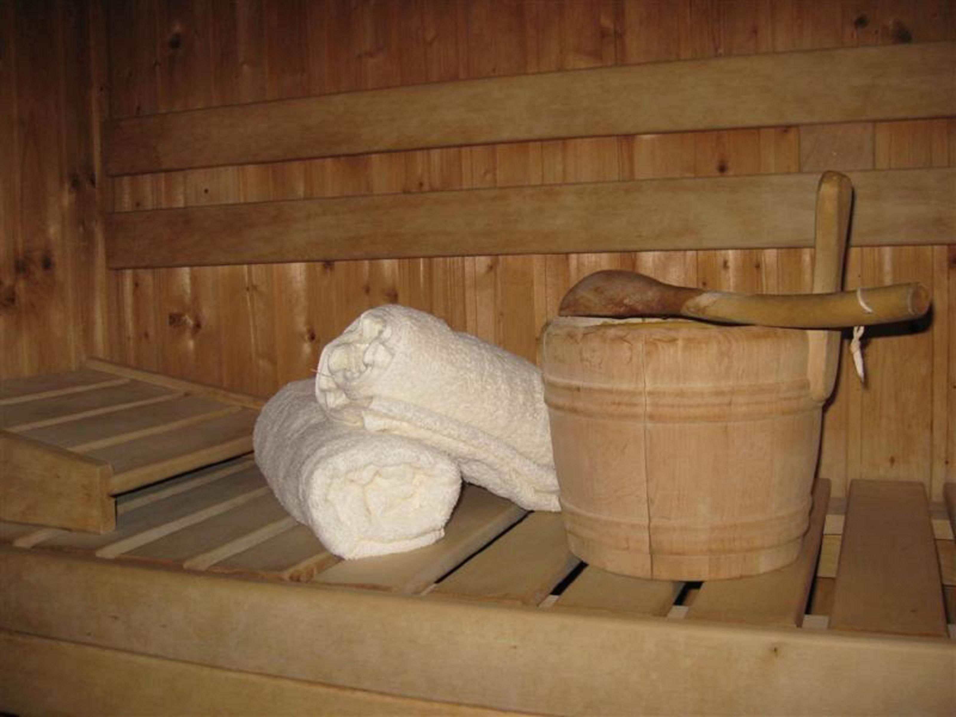 Uma sauna de madeira com um banco, um balde de madeira e uma toalha enrolada.