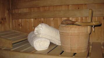 A wooden sauna with a bench, a wooden bucket, and a rolled-up towel.