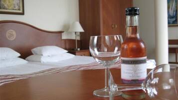 Una habitación de hotel con una cama, una mesita de noche, una lámpara y una mesa con una botella de vino y dos copas.