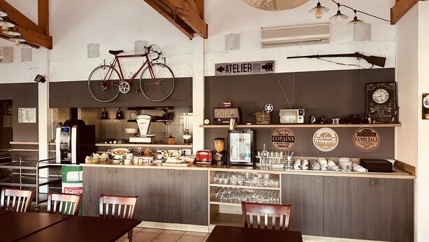 A café with wooden tables and chairs, a bar area with a variety of items, and a bicycle hanging on the wall.