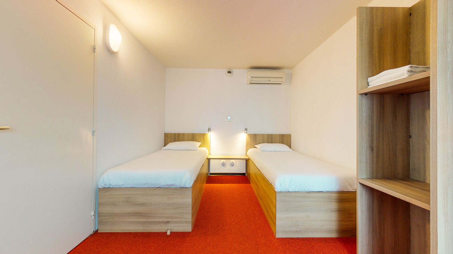 Een kleine, compacte kamer met twee eenpersoonsbedden, een rood tapijt, houten hoofdborden en een inbouwkast.