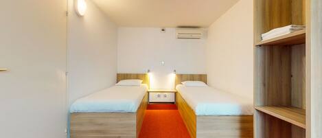 A small, compact room with two single beds, a red carpet, wooden headboards, and a built-in wardrobe.