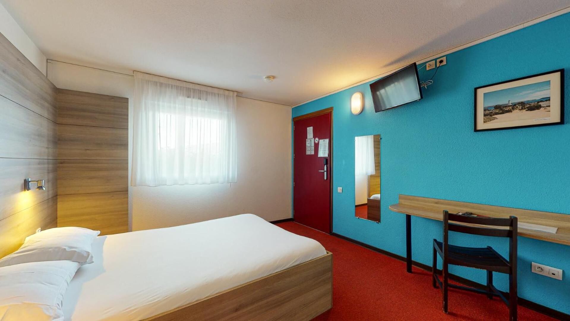 A hotel room with a bed, a desk, a chair, a TV, and a window with curtains.