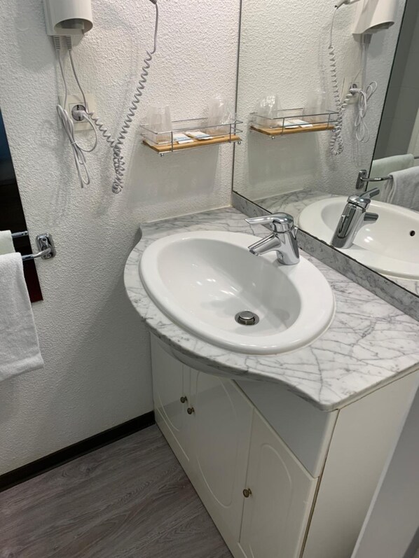 Un baño con lavamanos blanco, encimera de mármol y espejo. Hay dos toalleros y un estante con artículos de aseo.