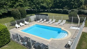 A rectangular swimming pool surrounded by a white fence, with several lounge chairs and a small covered seating area.