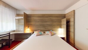 A modern hotel room with a large bed, bedside lamps, a wooden headboard, and a desk with a chair.