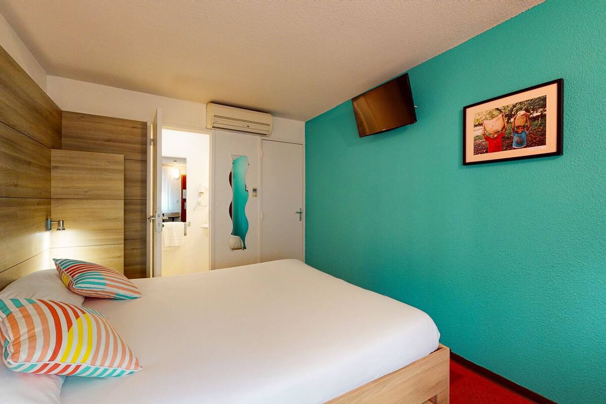 Un dormitorio con cama, almohadas, televisor y una puerta que da a un baño.