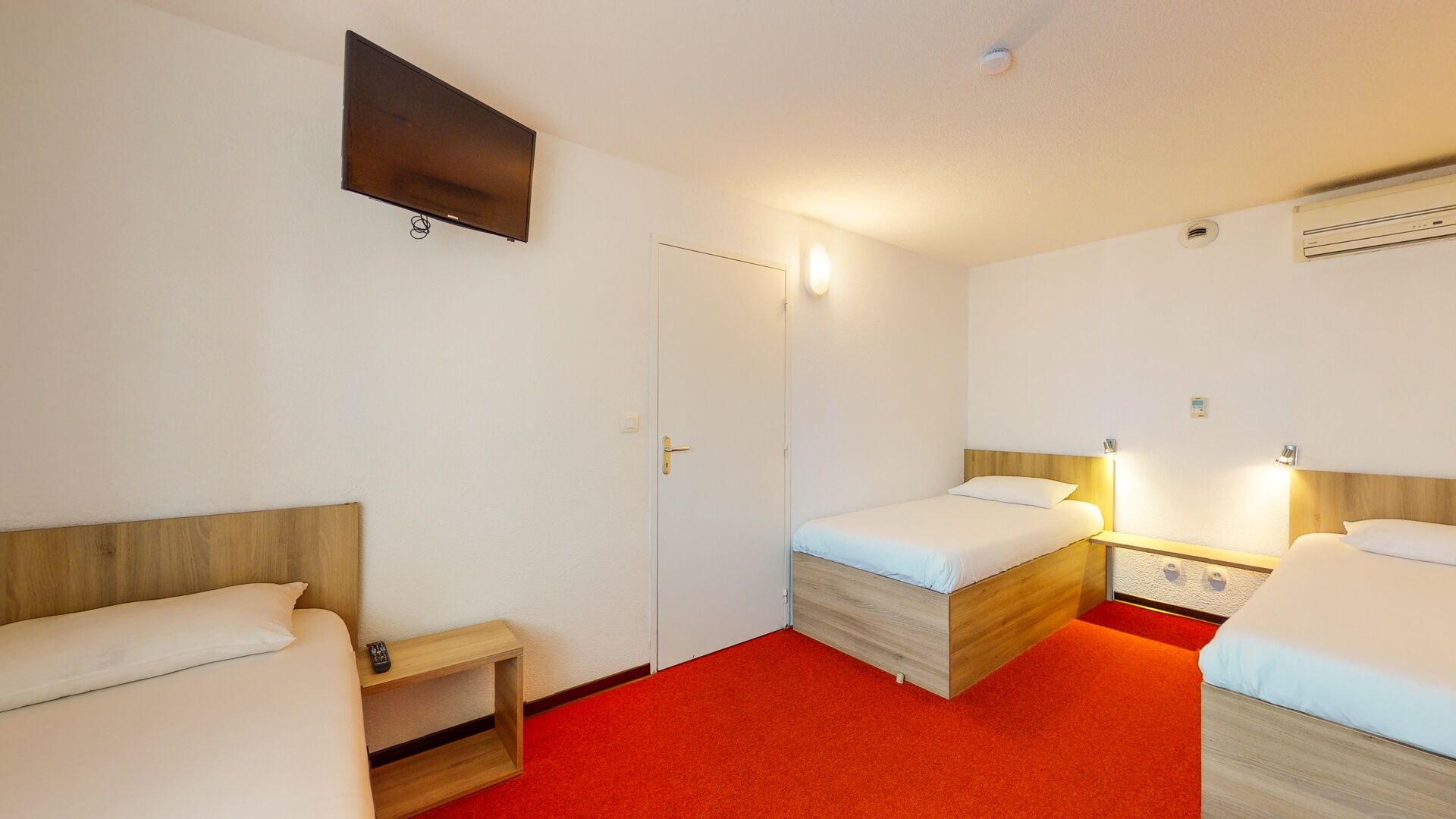Quarto de hotel com duas camas de solteiro, TV fixada na parede e piso com carpete vermelho.