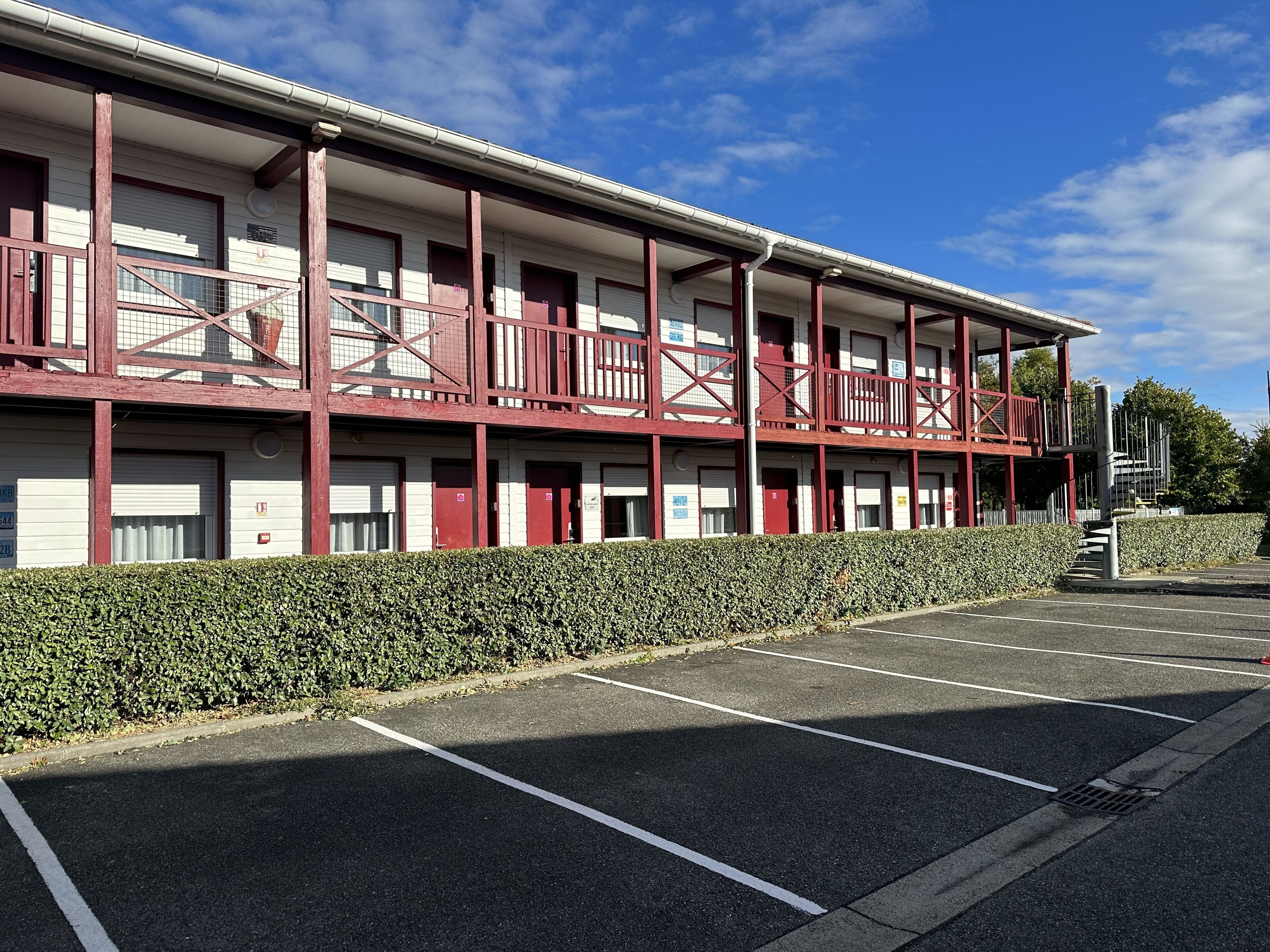 A multi-story building with a red exterior and white windows, featuring a parking lot in front.