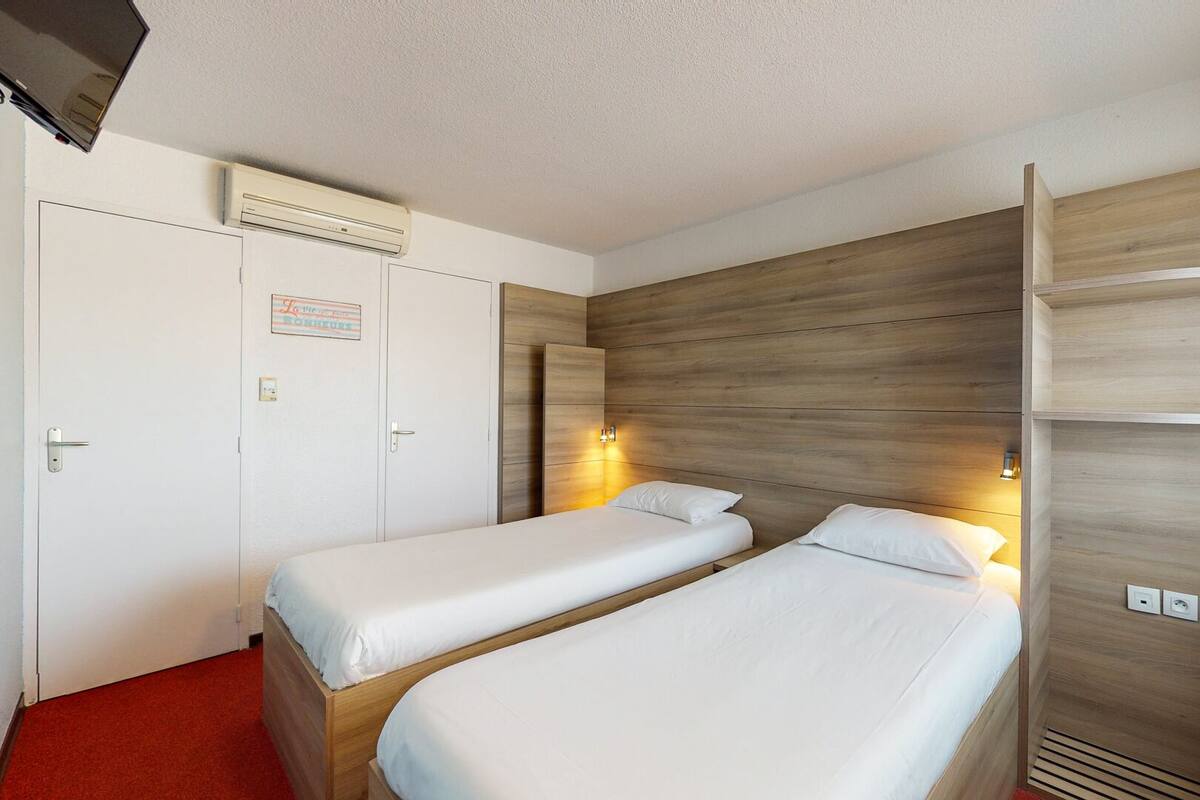 Habitación de hotel con dos camas individuales, un armario, un televisor y una pared de acento de madera.