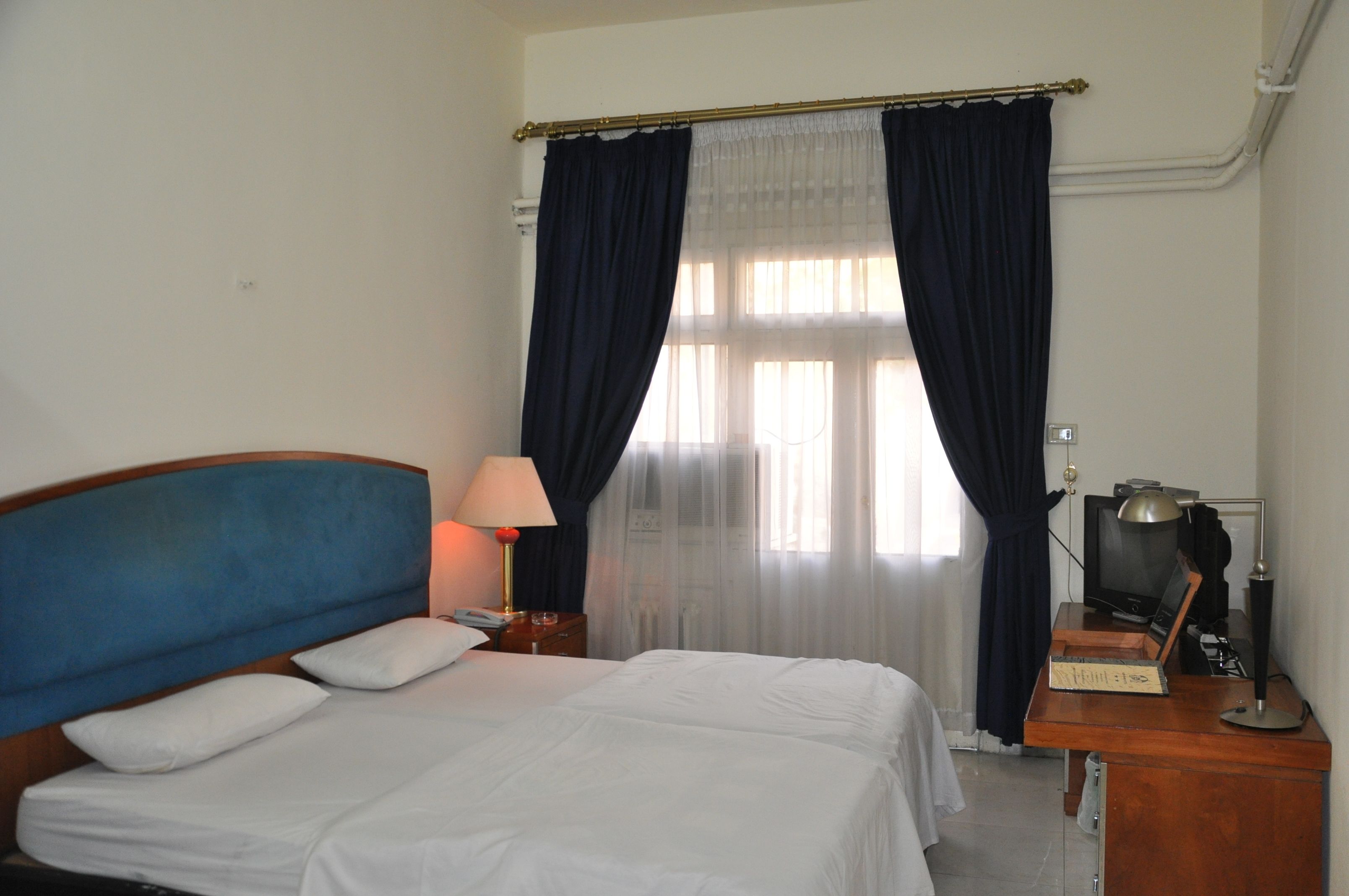 A hotel room with a bed, a desk with a computer, a lamp, and a window with curtains.