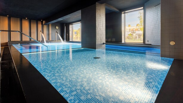 Une piscine intérieure à l’eau claire, dotée d’un plongeoir et de grandes fenêtres offrant une vue sur l’extérieur.