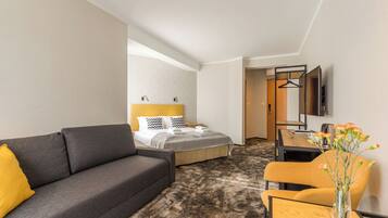 A hotel room with a bed, a sofa, a desk, and a TV.