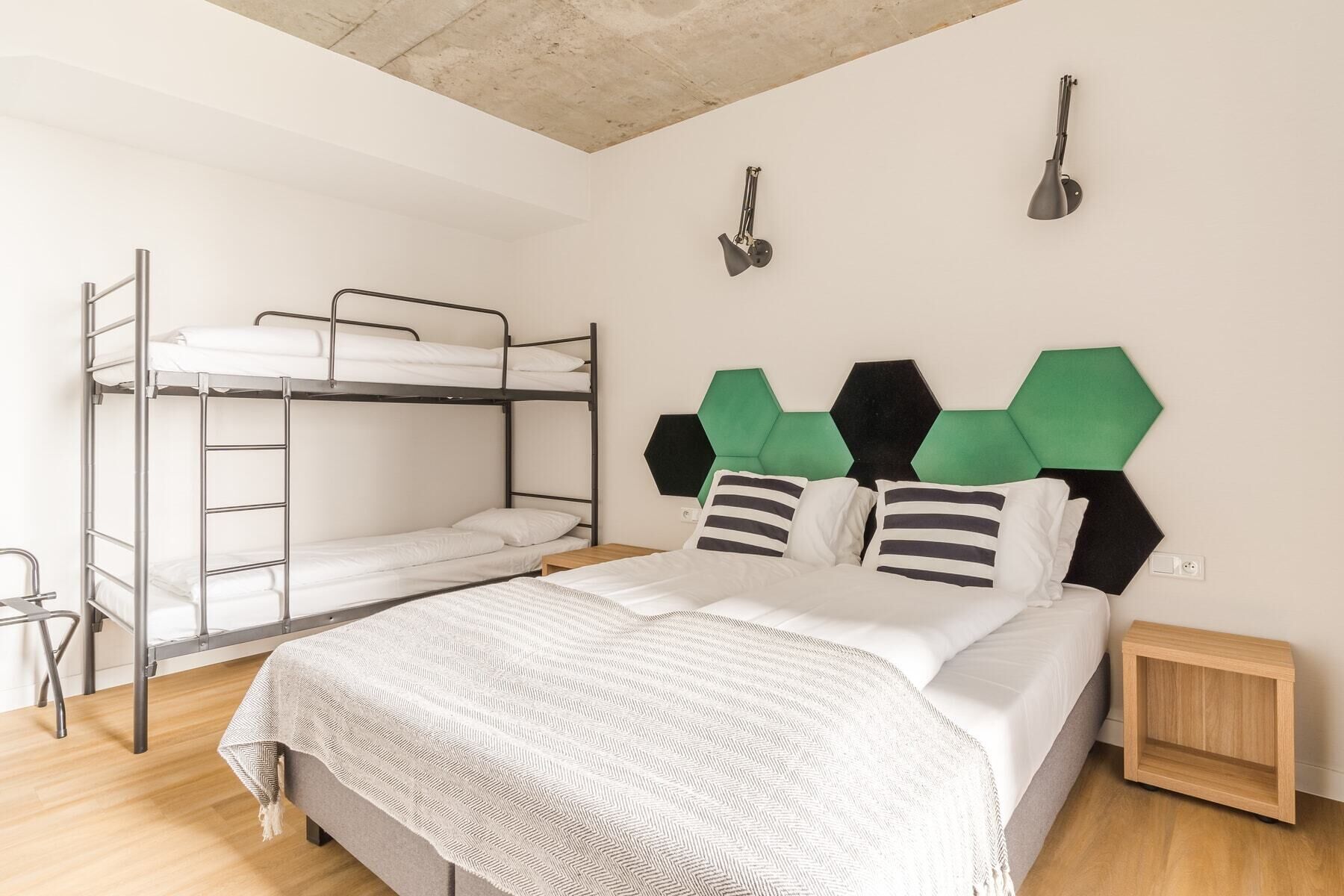 A bunk bed with a green and black geometric headboard, a bedside table, and a wall-mounted lamp.