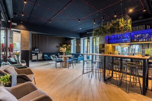 Un área de bar moderna con suelo de madera, taburetes y un espacio de estar con sofás y sillones.