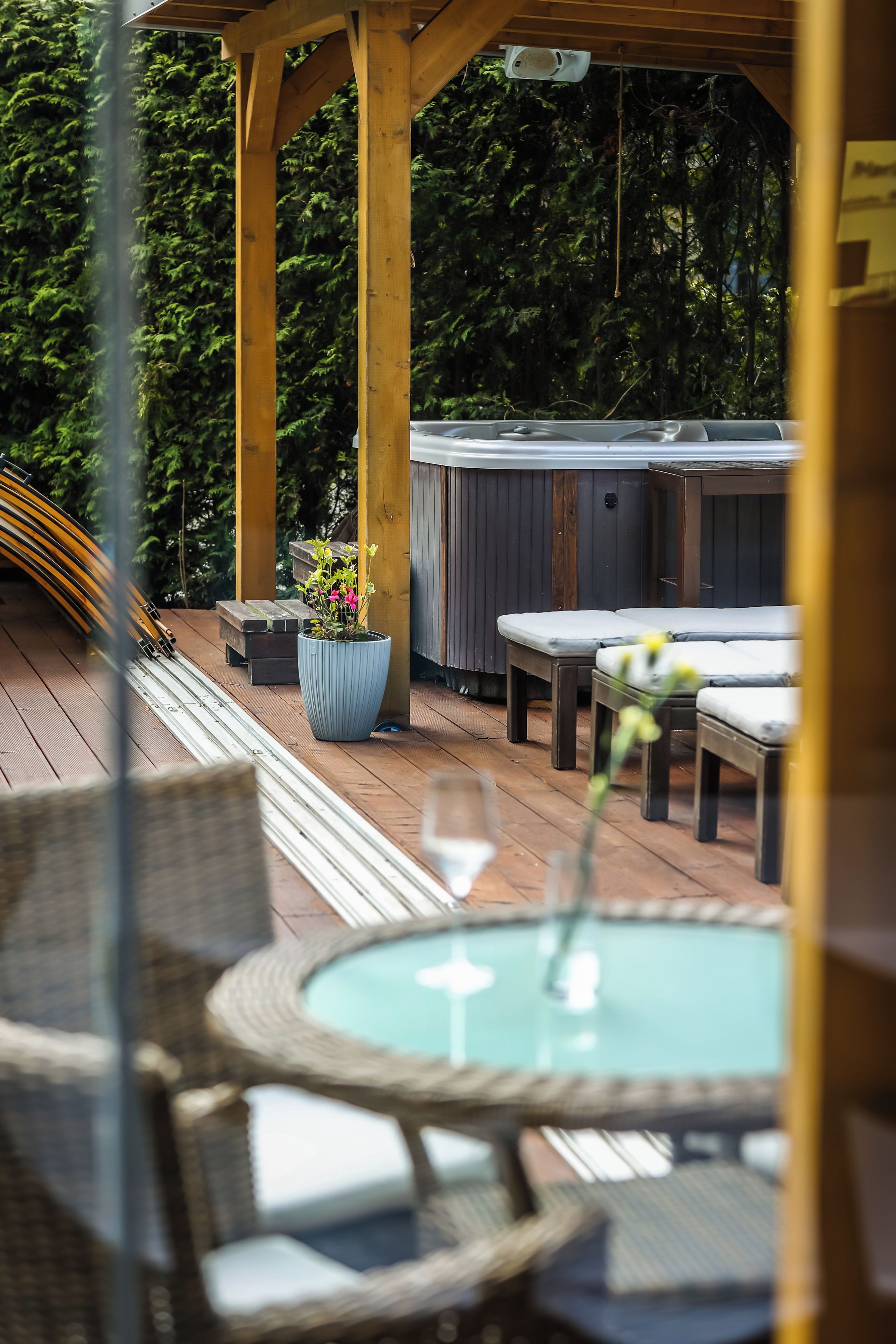 A wooden deck with a hot tub, lounge chairs, and a table with a glass.