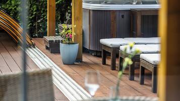 A wooden deck with a hot tub, lounge chairs, and a table with a glass.