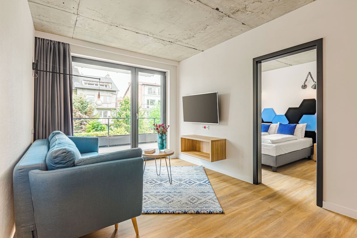 Un salon moderne avec un canapé, un téléviseur fixé au mur et une vue sur l’extérieur grâce à de grandes fenêtres.