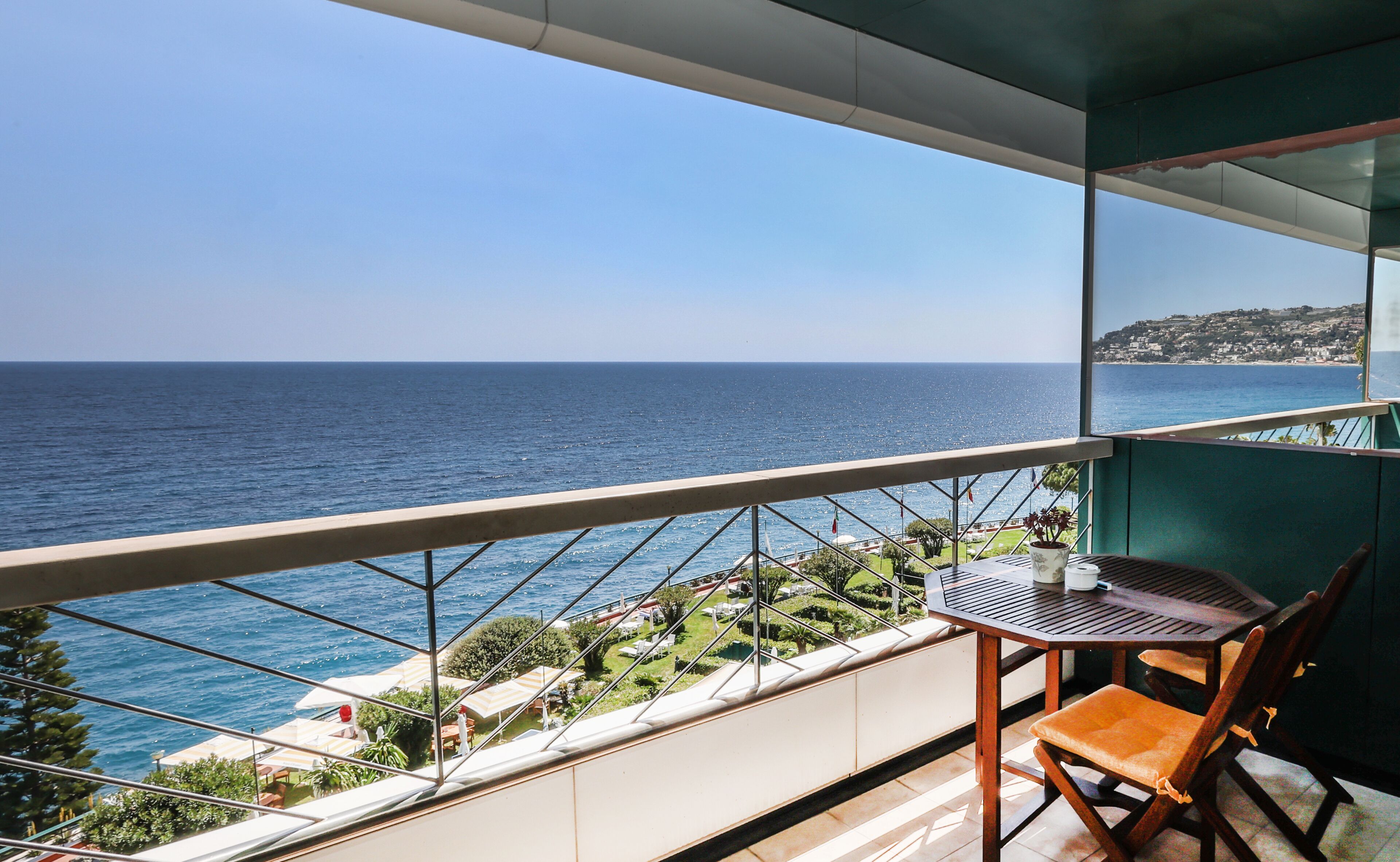 A balcony with a view of the sea, a table, and a chair.