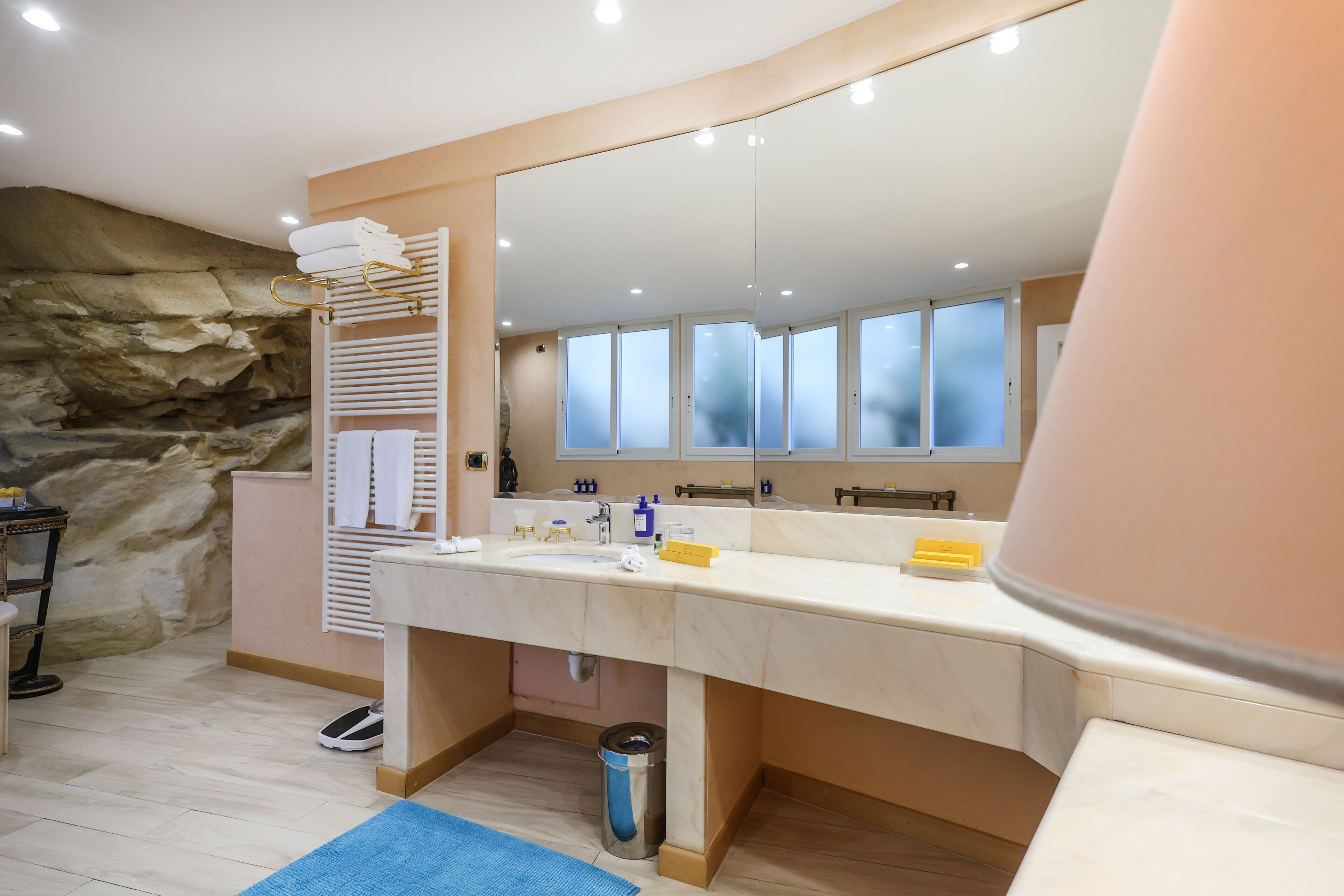 Un baño con un espejo grande, un lavabo, un perchero para toallas y una pared de piedra.