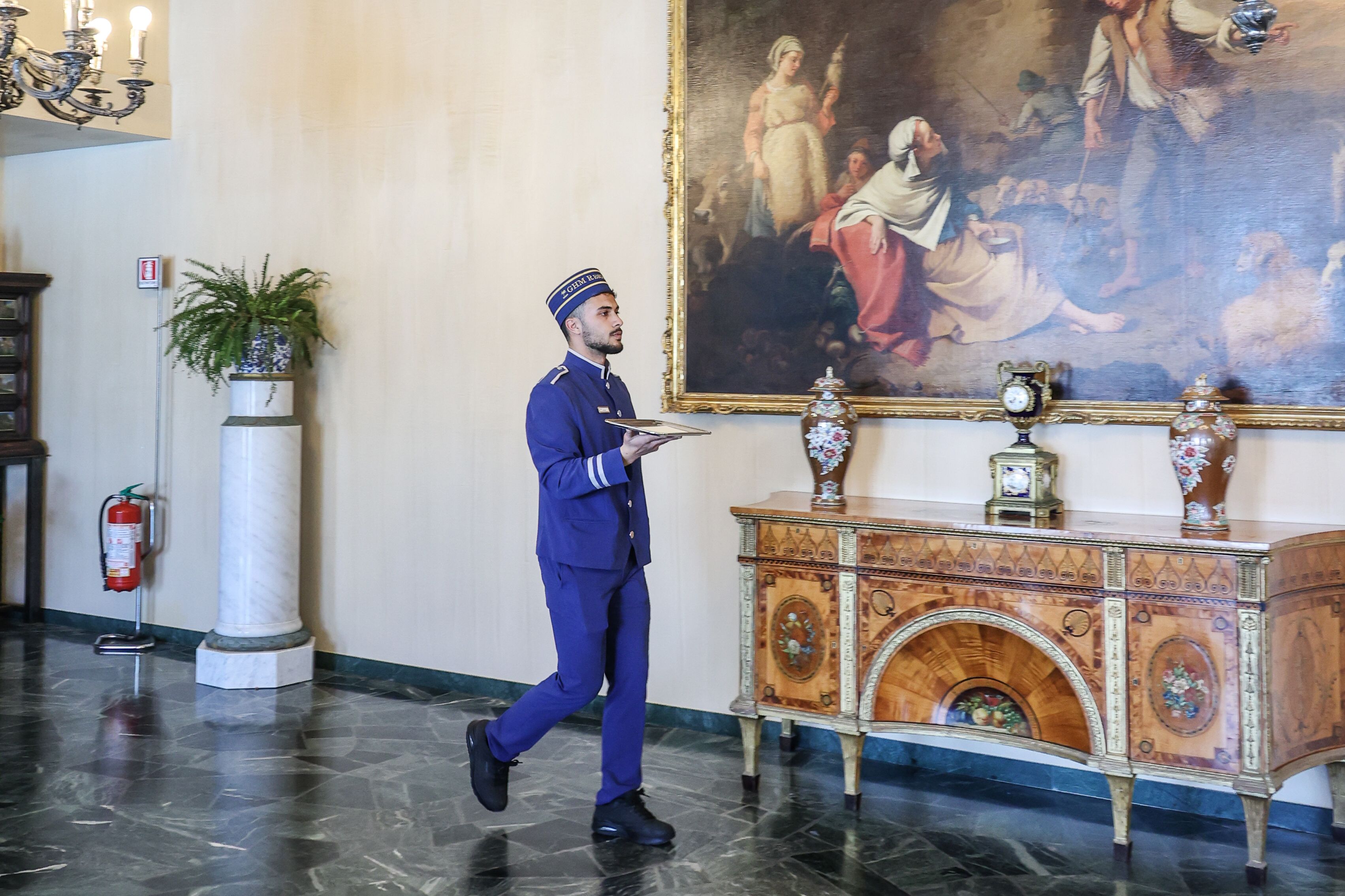 Un'accogliente hall d'hotel con pavimento in marmo, un grande quadro appeso al muro, un mobiletti in legno decorativo e un estintore.