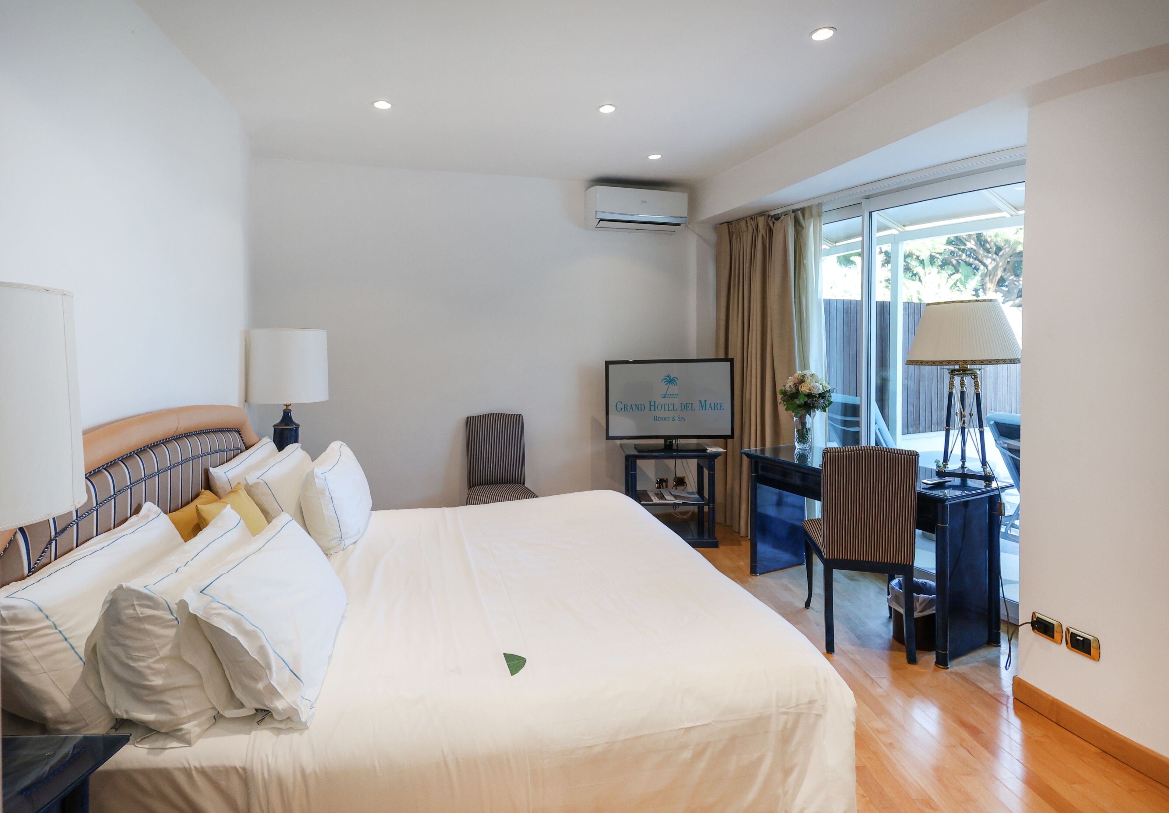 A hotel room with a large bed, a desk with a computer, a television, and a window with curtains.