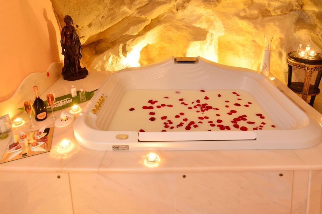 Ein Spa-Ambiente mit einer Badewanne, Rosenblüten, Kerzen und einer Statue.