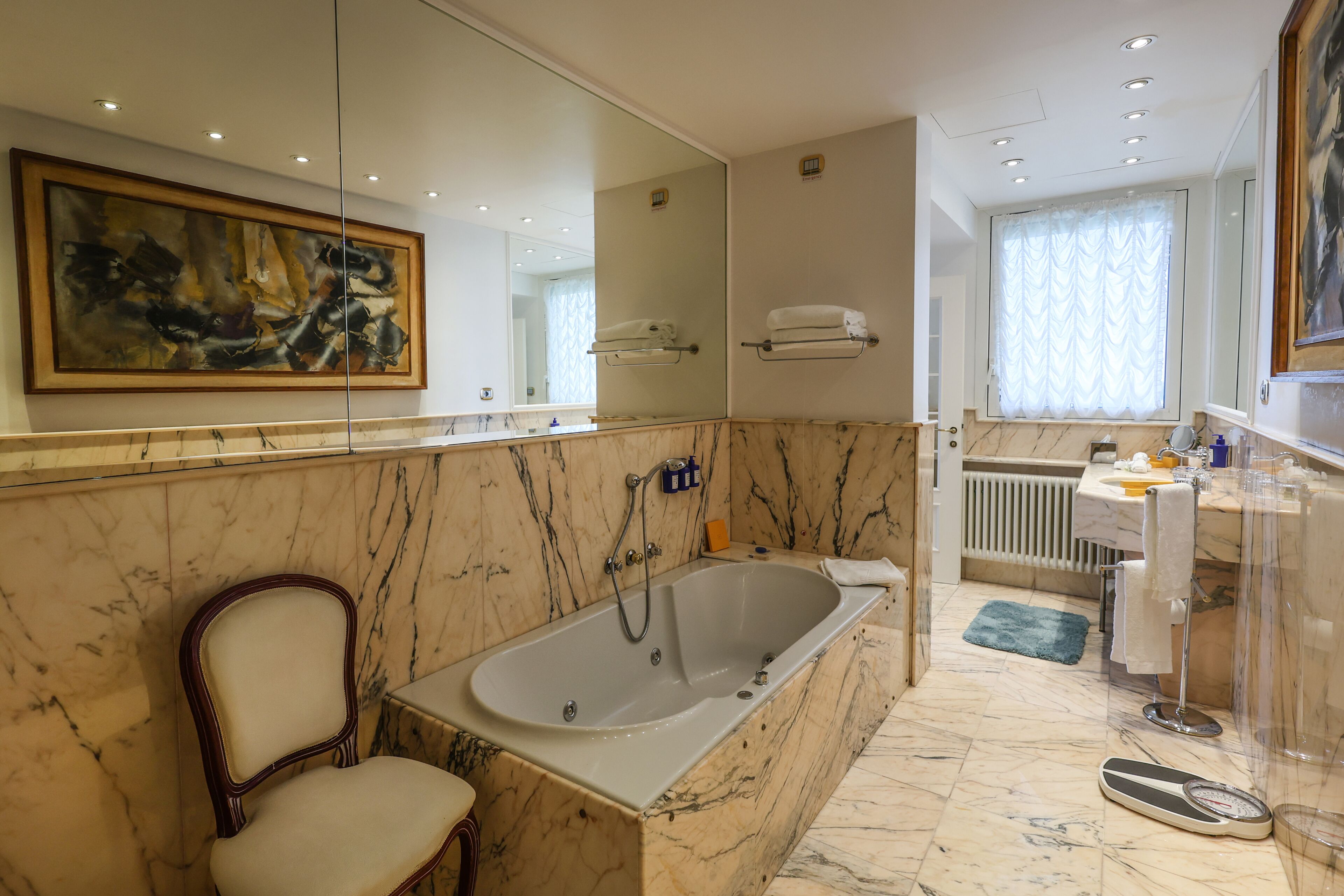 A bathroom with a large bathtub, a chair, a scale, and a mirror.