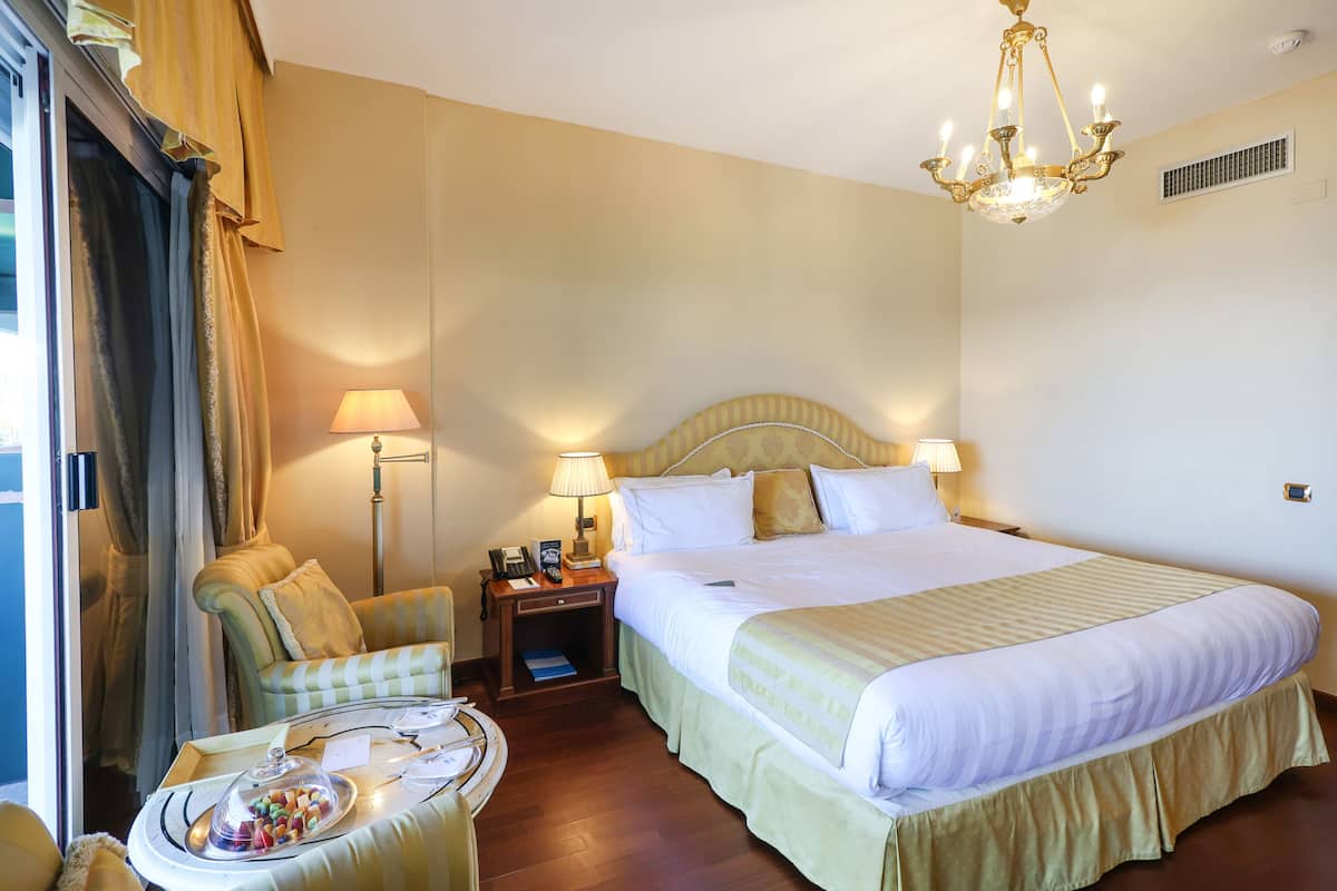 Ein Hotelzimmer mit einem großen Bett, Nachttischlampen, einem Sessel, einem kleinen Tisch mit einer Snackplatte und einer Chandelieber.
