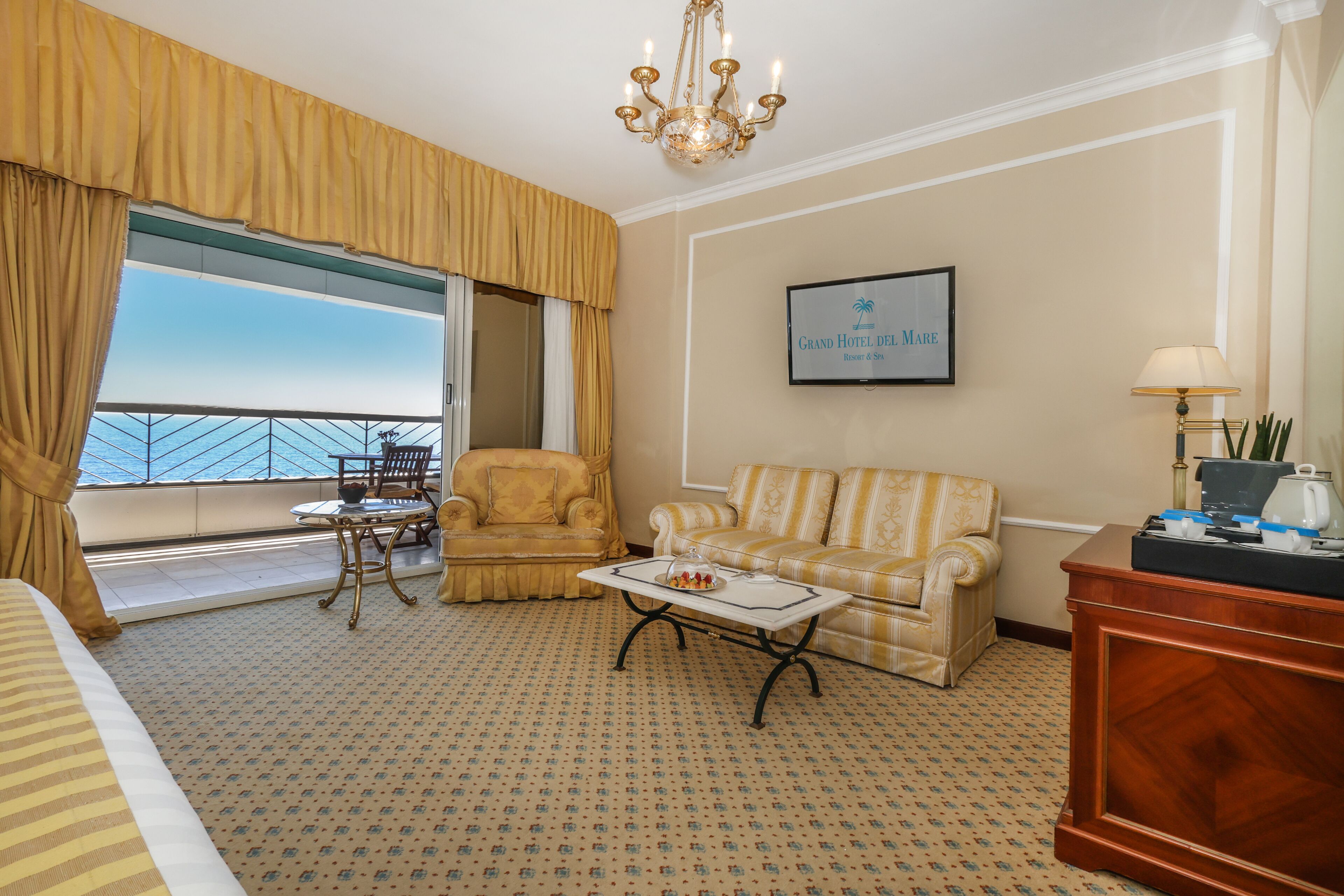 Una habitación de hotel con balcón, un sofá, una silla, una mesa de centro y un escritorio.