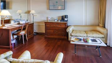 A hotel room with a wooden desk, a sofa, a coffee maker, and a framed sign on the wall.