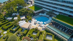 An aerial view of a hotel with a swimming pool, outdoor seating, and a well-maintained garden.